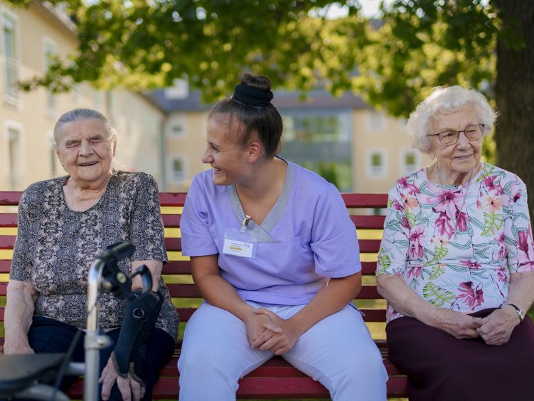 Eine Pflegerin unterstützt Bewohner/innen beim Kartenspiel auf der Terasse