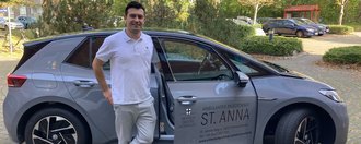 Pfleger steht vor einem Auto des Mobilen Pflegedienstes St. Anna.