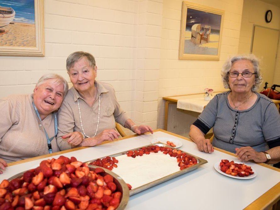 drei Frauen an einem Tisch mit Erdbeeren - lächeln in die Kamera